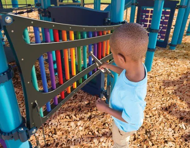 Child playing with colorful chimes on a playground surrounded by blue play structures.