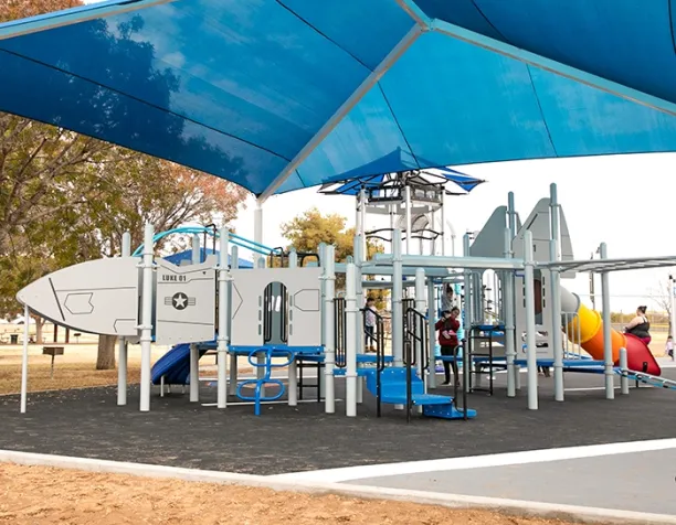 Children play on a space-themed playground structure under a large blue shade canopy.