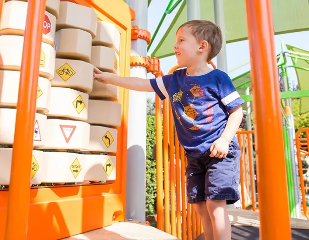 Young child in blue shirt interacts with educational game panel featuring traffic symbols.