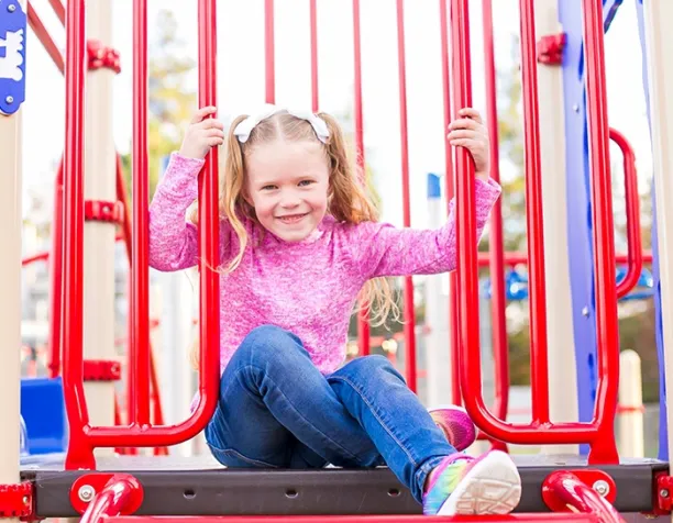 Smiling girl in pink on playground sitting between red bars.