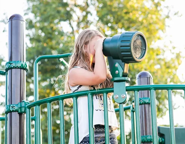 Girl looking through green periscope on playground equipment platform.