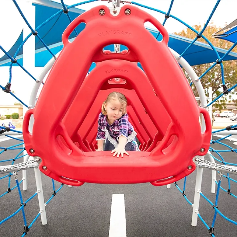 Girl crawling through a series of red climbing pods on a playground structure.