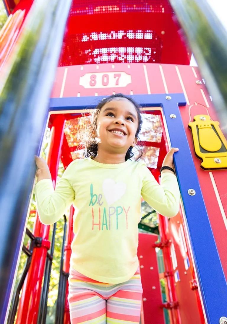 Smiling girl with a yellow shirt in a red playground structure.