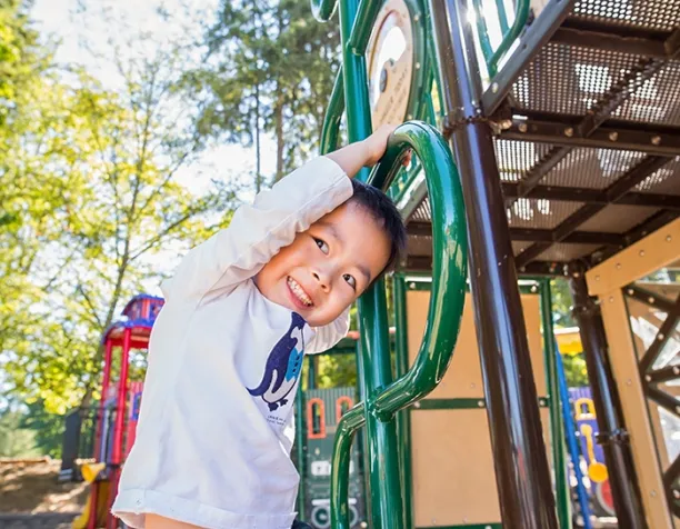 Smiling child hanging on a green climbing bar under a sunny sky.