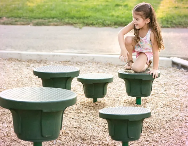 Young girl climbing on green stepping pods in a sunlit playground.
