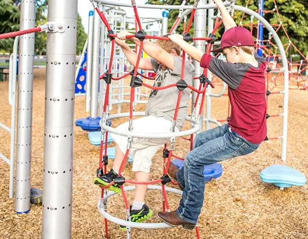 Two boys climbing on a vertical rope net structure on a sunny day.