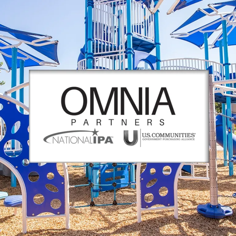 Blue and white playground with climbing structures and shade sails, set in a sunny area with wood chip surfacing.
