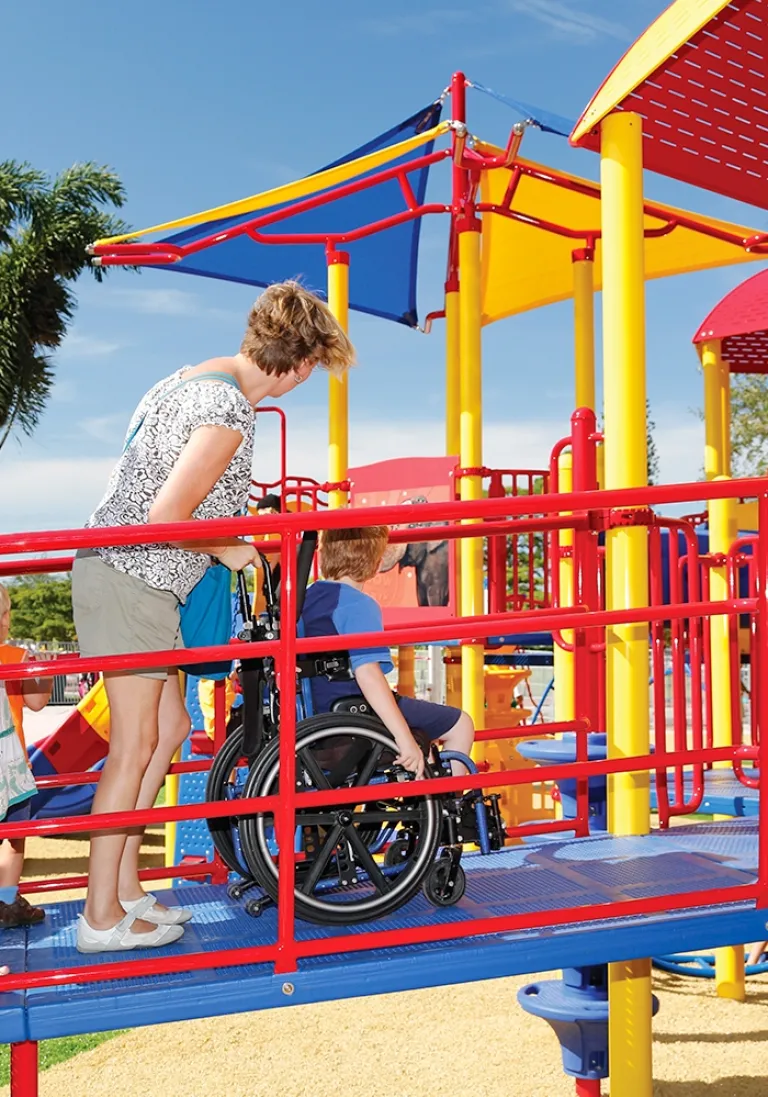 Child in a wheelchair navigating a ramp on an inclusive playground.
