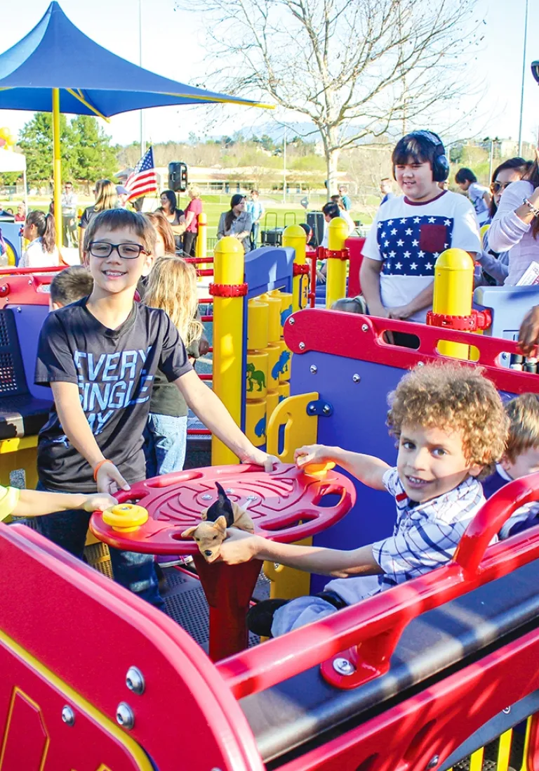 Children engaging with interactive panels on a colorful playground structure under sunny skies.