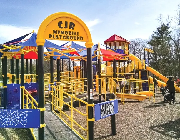 Playground with multiple slides, ramps, and colorful shade sails on a sunny day.