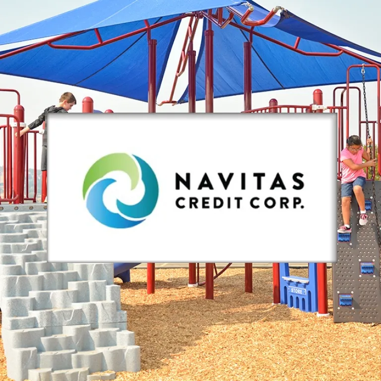 Kids climb a play structure with a blue shade canopy on a sunny day.