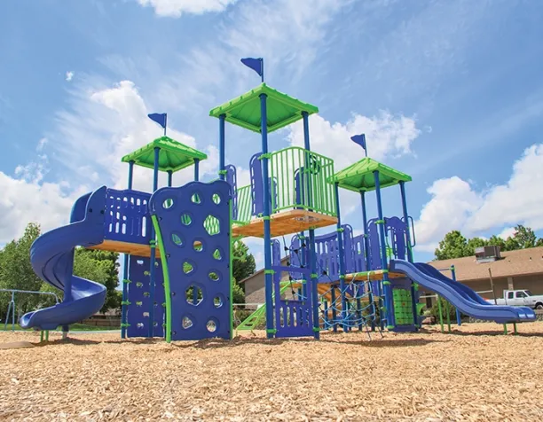 Colorful playground structure with blue slides and green roofs on a sunny day.