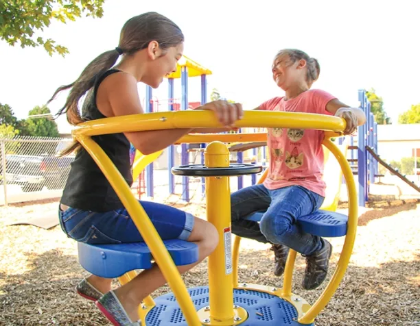 Two children laughing while spinning on a yellow and blue merry-go-round.