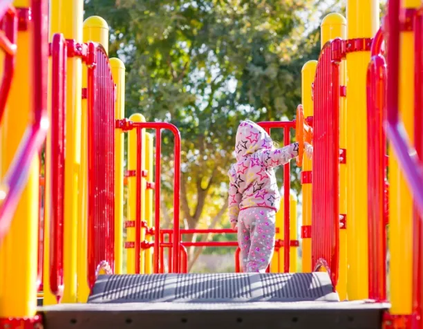 Child in star-patterned outfit on a playground bridge surrounded by red and yellow structures.