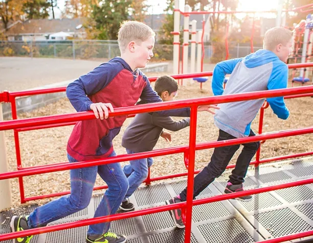 Three boys running across a red metal bridge on a playground.