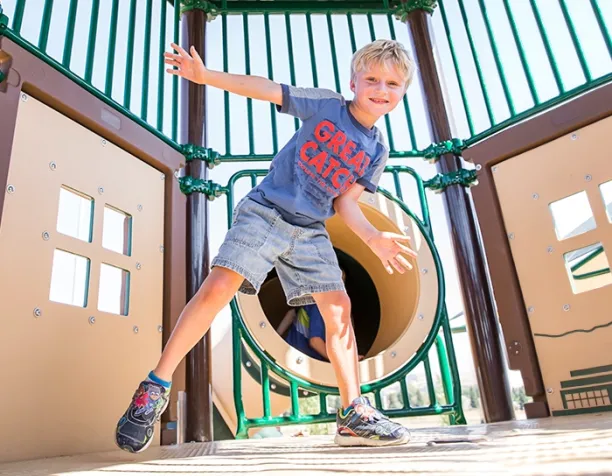 Smiling child balancing inside a play structure with tan and green panels.
