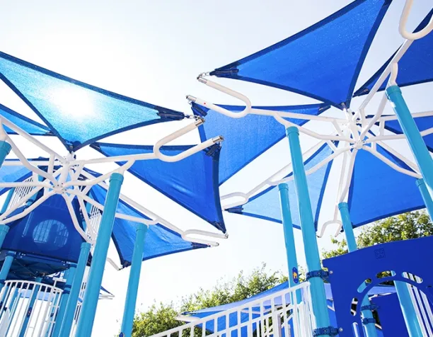 Blue and white shade structures over a playground on a sunny day.