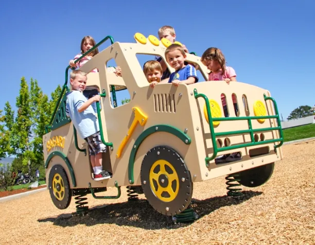 Children play on a beige truck-shaped playground structure in a sunny area with wood chip surfacing.