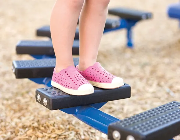 Child's feet in pink shoes balancing on blue playground equipment.