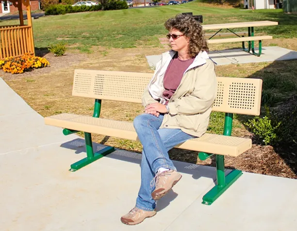 Person sitting on a beige bench with green supports in a sunny park area.
