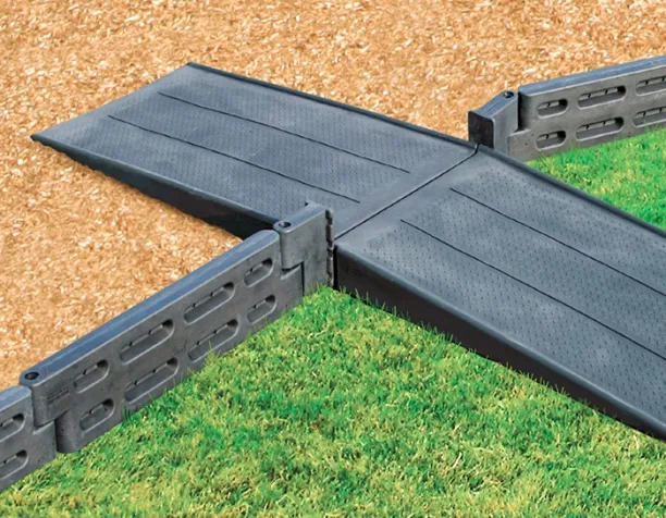 Interlocking black playground borders with ramps on grass and wood chips.