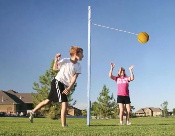Two children playing tetherball on a grassy field under a clear blue sky.
