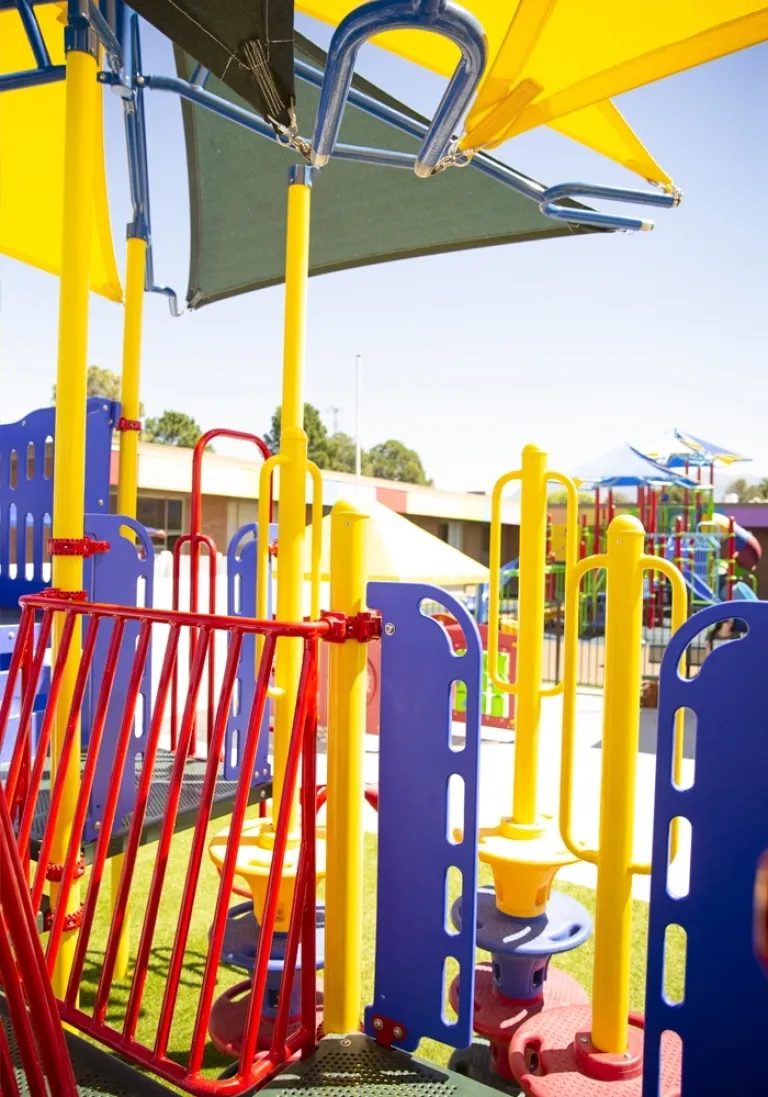 Brightly colored playground equipment with slides and shade structures under a sunny sky.