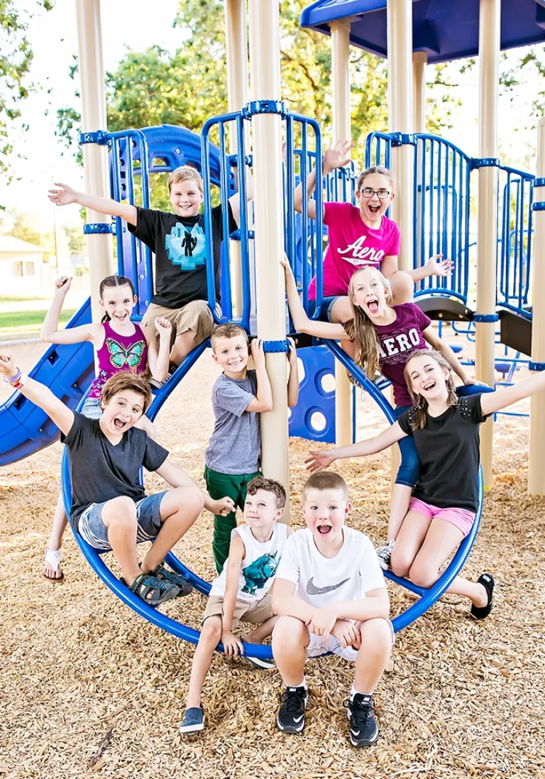 Group of children posing energetically on blue playground structure with wood chip surfacing.