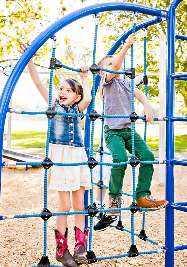 Two children climbing a blue rope net structure on a sunny day.