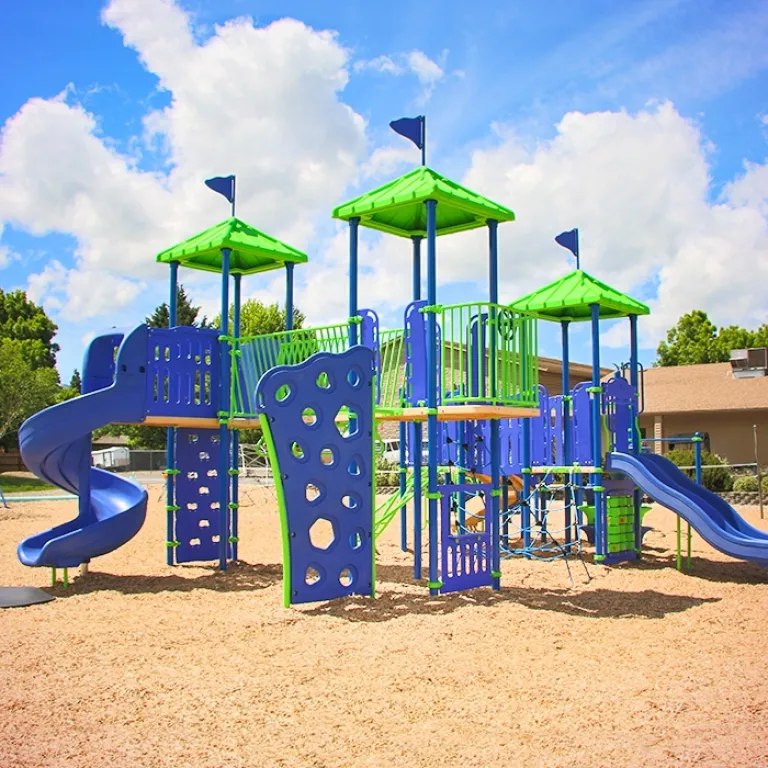 Colorful playground with green and blue climbing structures and slides under a partly cloudy sky.