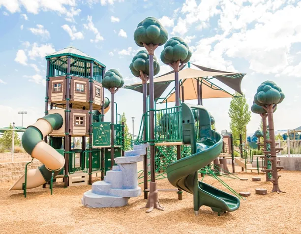 Multi-level play structure with slides and tree-themed poles on a sunny day.