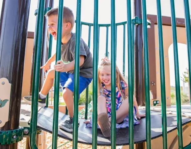Two children playing inside a playground tube with vertical bars, smiling and having fun.