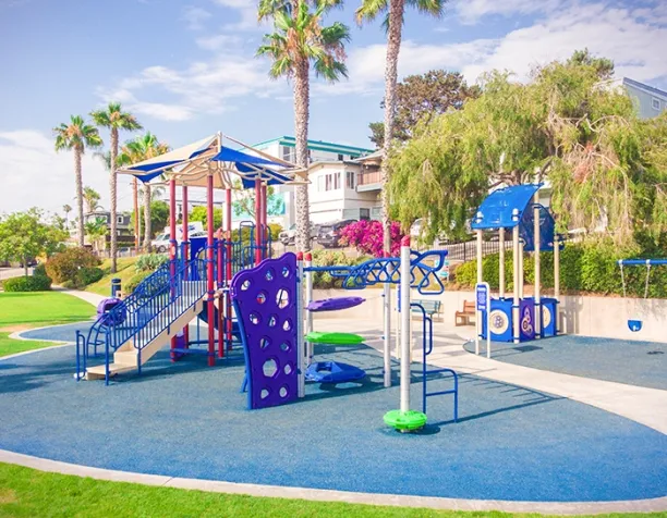 Colorful playground with slides and climbing structures under a clear sky, surrounded by palm trees.