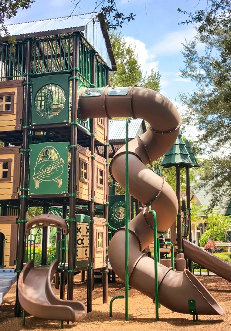 Large playground structure with brown spiral tube slide and green panels under a clear sky.