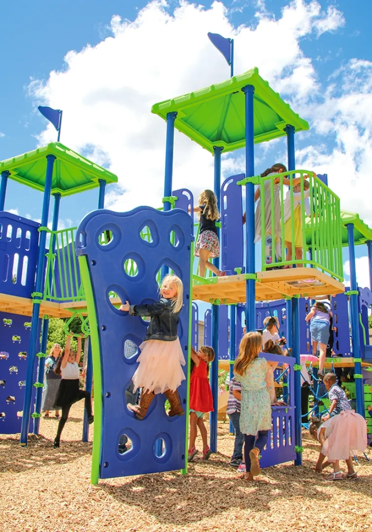Children climbing on colorful play structure with blue and green panels against a bright sky.