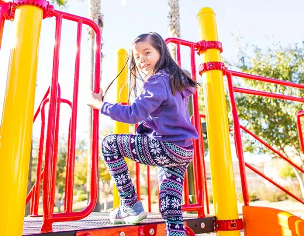 Smiling girl climbing red and yellow playground stairs in sunny weather.