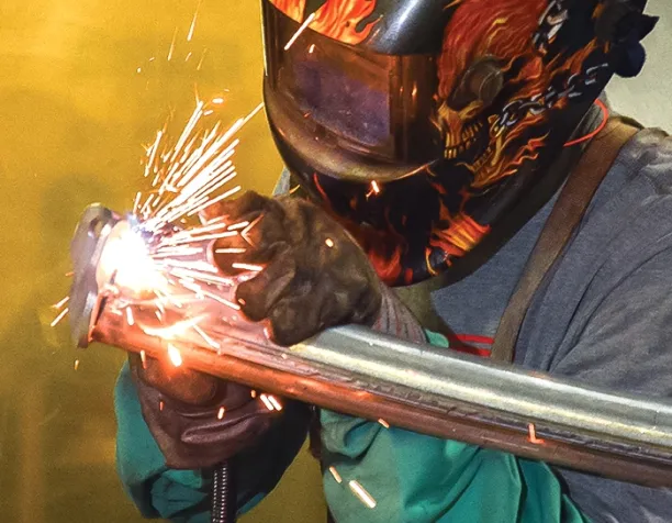 Person welding metal with a helmet featuring a flame design.