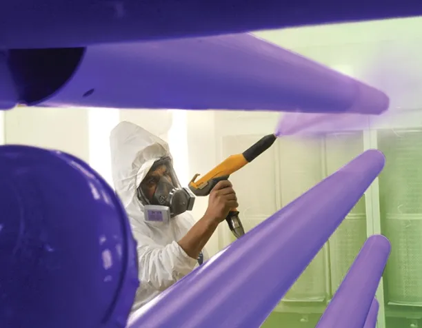 Person in protective gear spraying purple paint on metal pipes.