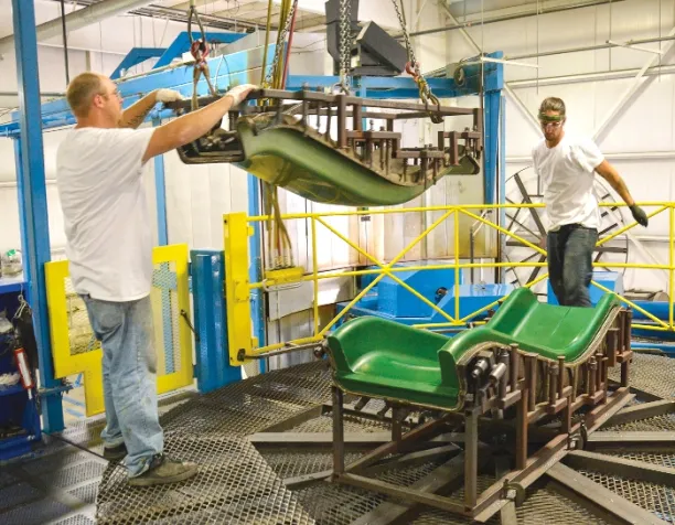 Two men in a factory assembling a green plastic playground slide with metal framework.
