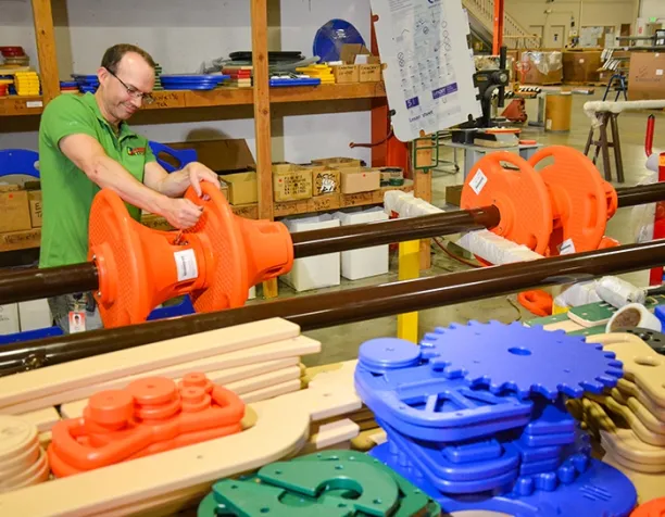 Man in a green shirt assembling orange playground equipment in a workshop.