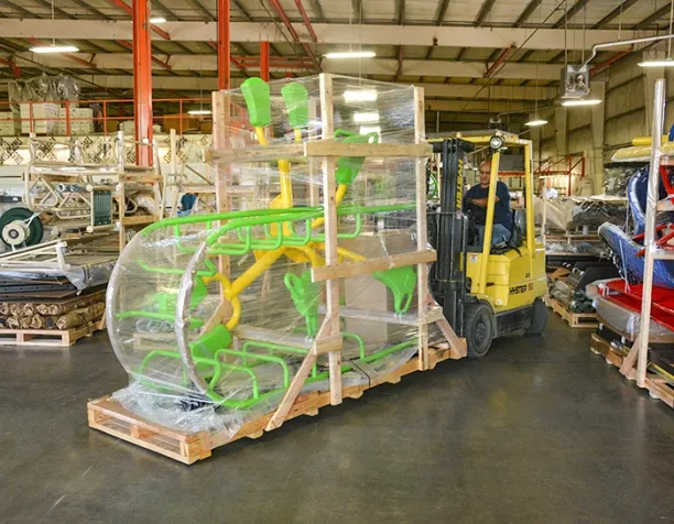 Forklift in a warehouse moving a wrapped green and yellow playground structure.