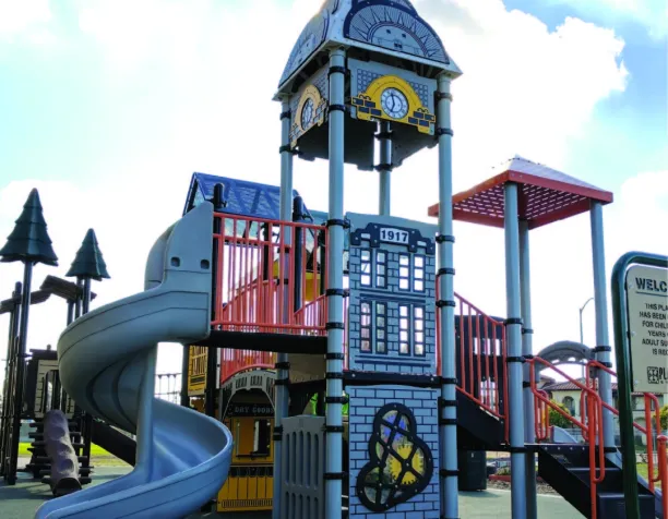 Colorful playground tower with a spiral slide and clock-themed design under a blue sky.